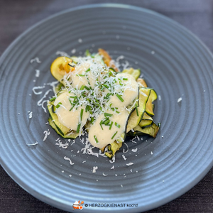 Zucchini Carpaccio - gebraten mariniert mit Parmesan Zabaione auf schwarzem Teller