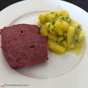 Eine Scheibe hausgemachter Leberkäs mit Kartoffelsalat auf einem weißen Teller