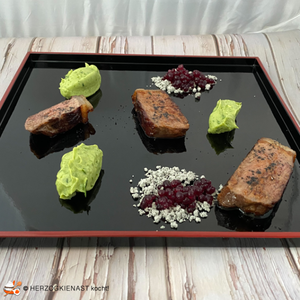 Roastbeer mit Avocado, Trüffelpuder und Rotweinkaviar auf einem schwarzen Teller