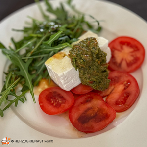 Ein dickes Stück Feta auf Tomatenscheiben mit Kubenpfeffer Salsa und Rucola