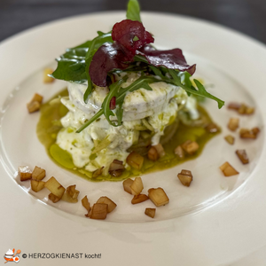 Kohlrabitürmchen mit Kohlrabisalat und Wildkräutern getoppt und auf weißem Teller angerichtet