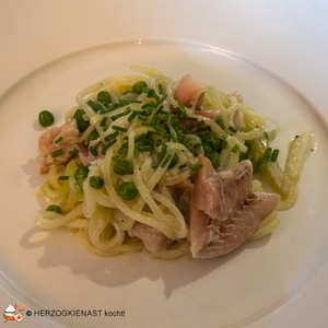 Kohlrabinudeln mit Erbsen und Fischfilet auf weißem Teller angerichtet